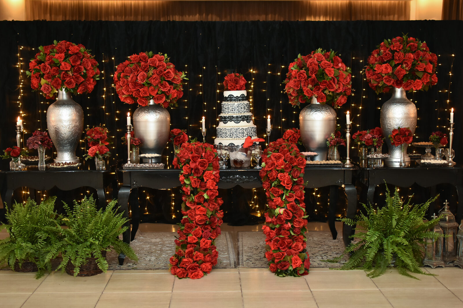 Decoração de mesa com arranjos florais vermelhos e bolo do evento